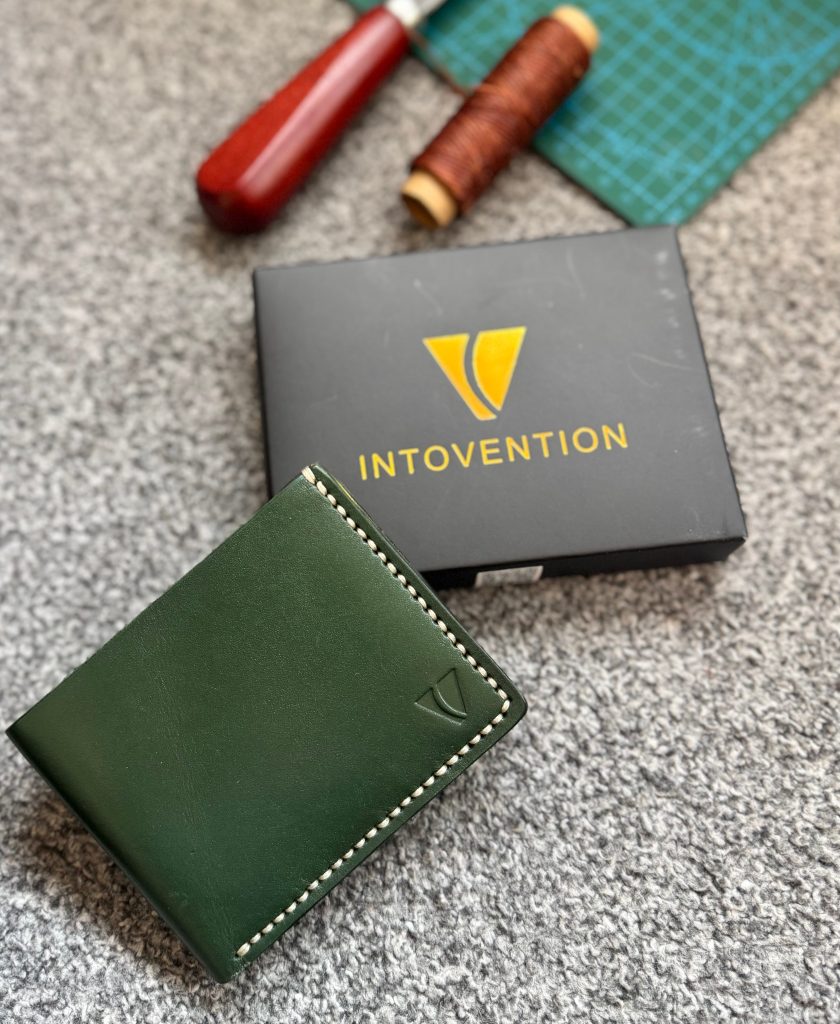 Intovention packaging, craft tools, thread, and handmade wallet on a workbench