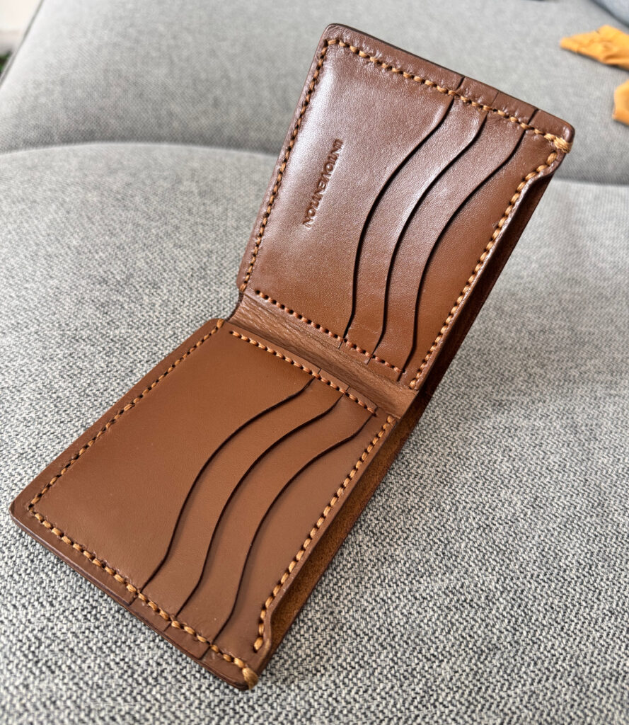 Brown handmade leather bifold wallet opened on grey fabric with visible card pockets.