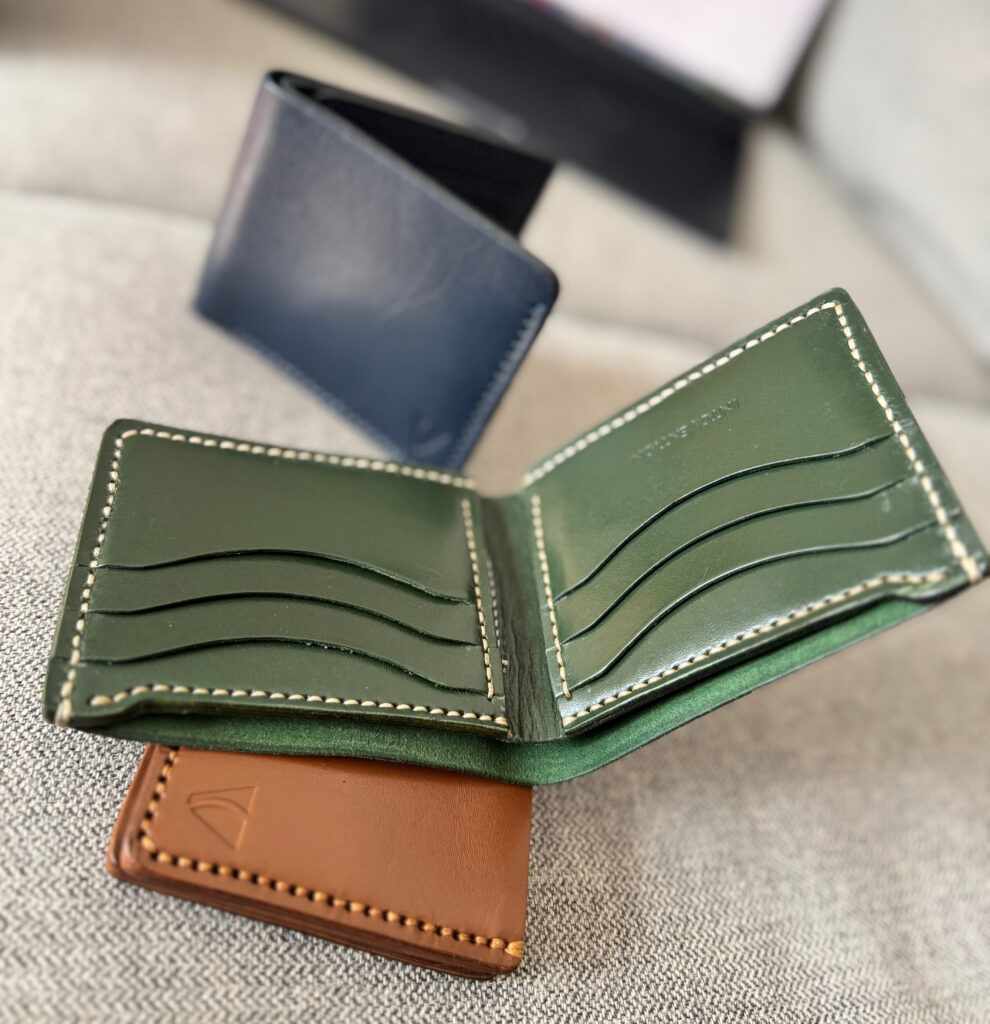 Forest green handmade leather bifold wallet opened with visible card pockets and cream stitching.