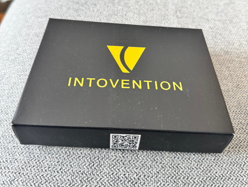 Black Intovention packaging box with gold logo on grey fabric.